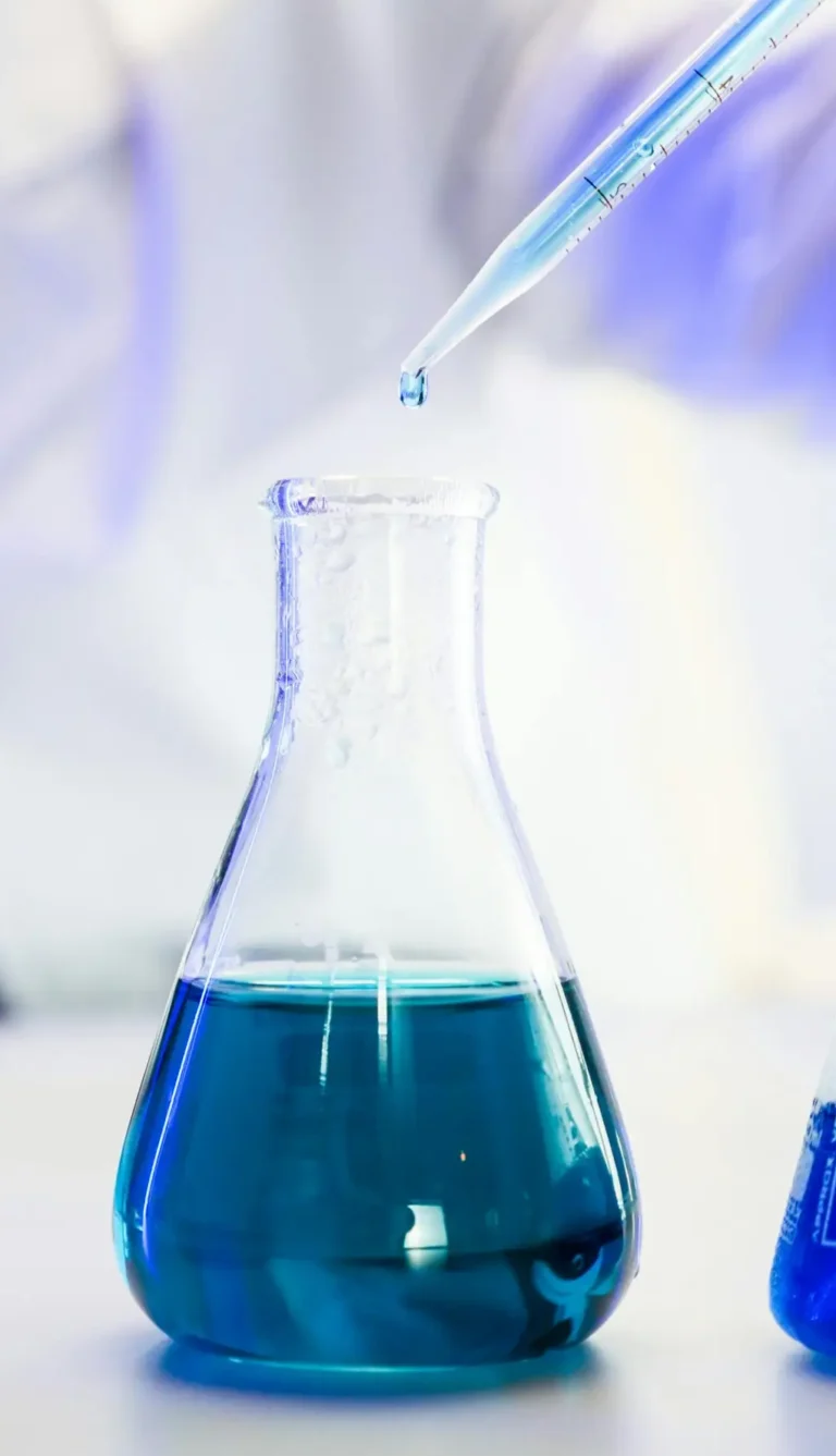 Close-up of blue liquid in Erlenmeyer flask with pipette in a modern lab setting.